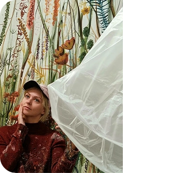 Kasia in red sweater in front of colorful botanical mural.