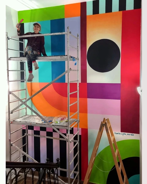 Kasia painting colorful geometric mural on wall.