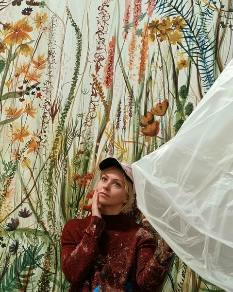 Kasia in red sweater in front of colorful botanical mural.